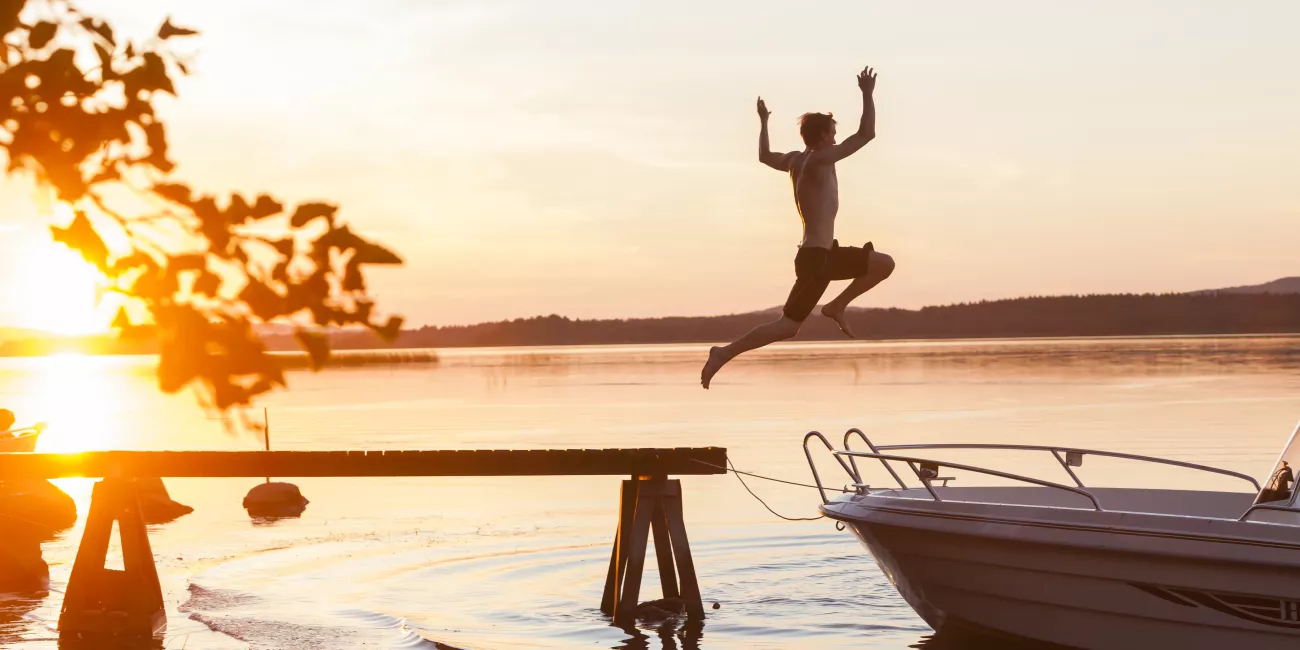 A boy jumping from a pier into a lake against the backdrop of the setting sun