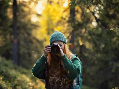 A young woman taking photos with a camera in an autumn forest