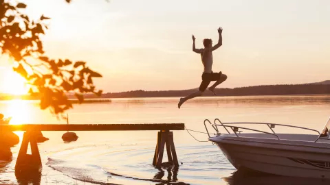 A boy jumping from a pier into a lake against the backdrop of the setting sun